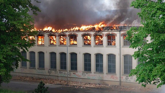 Flammen schlagen aus einem Industriegebäude mit eingestürztem Dach