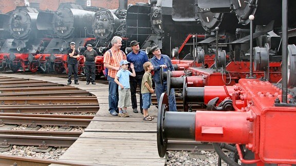 Fünf Männer und zwei kleine Kinder stehen einem Kreis aus Dampflokomotiven.