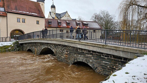 Ein stark angestiegener Bach unter einer Brücke, die zum Wasserschloss Klaffenbach führt.