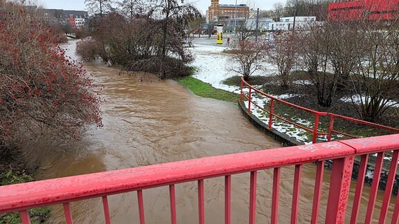 Blick von einer Brücke auf einen Bach neben einer Straße, der über die Ufer getreten ist.