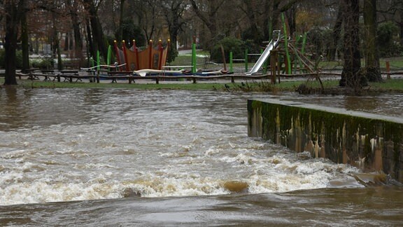 Tosendes Wasser eines Baches vor einem Spielplatz.