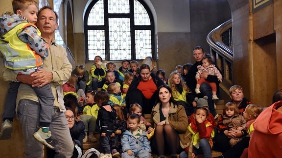 Kindergartenkinder und Erzieherinnen sitzen traurig auf einer Treppe im Rathaus Chemnitz 