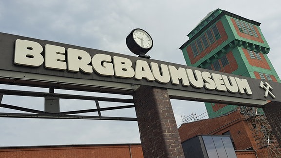 Kohlewelt 2: Auf einem Schild steht "Bergbaumuseum". Im Hintergrund ist ein großer Turm zu sehen.