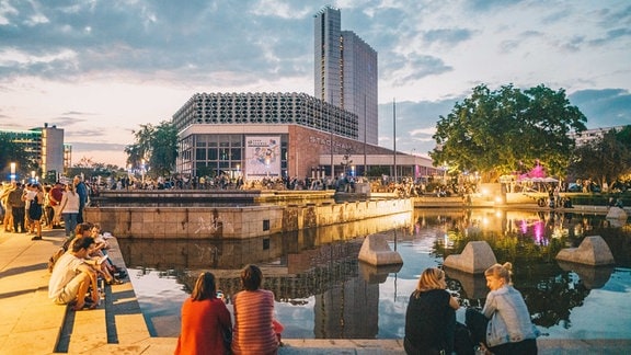 Im Abendlicht tummeln sich viele Menschen am Wasser in einer Innenstadt.