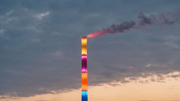 Ein bunt leuchtender Schornstein ragt über eine Stadt hinaus.