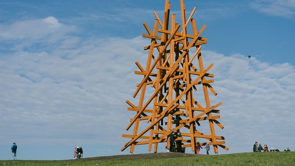 Ein überdimensionale Holzskulptur steht auf einer grünen Wiese.