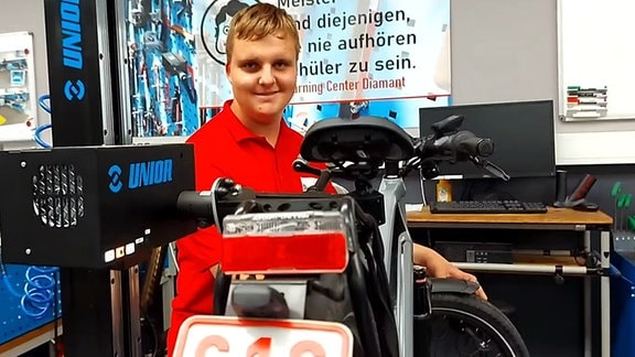 Ein E-Bike ist aufgebockt an einer Werkbank zu sehen. Daneben steht ein junger Mann und hat Werkzeuge in der Hand. Es sit ein Lehrling im ersten Ausbildungsjahr bei der Firma Diamant Fahrradwerke GmbH in Hartmannsdorf. 