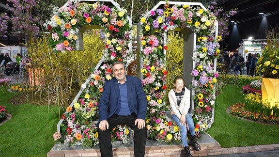 Andreas Richter sitzt mit einem Mädchen vor einer mit Blumen gestalteten "20".