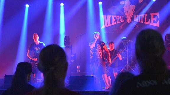 Zuschauer blicken zu einer Bühne, auf der eine Metal-Band spielt.