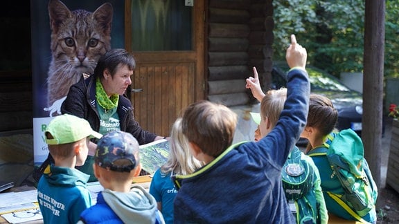 Eine ältere Frau zeigt einer Kindergruppe ein Bild. Darunter melden sich zwei.