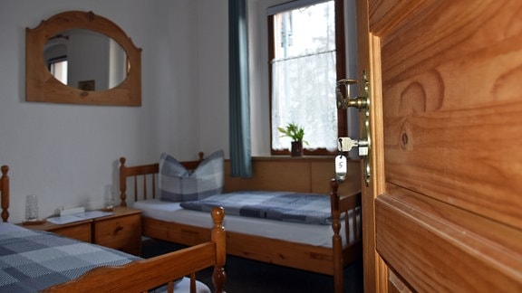 Blick in ein Pensionszimmer, am Schloss der offenen Tür hängt ein Zimmerschlüssel. 
