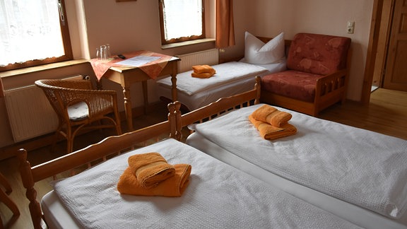 Auf den zwei Betten und einem Zustellbett in einem Pensionszimmer liegen gefaltete Handtücher.
