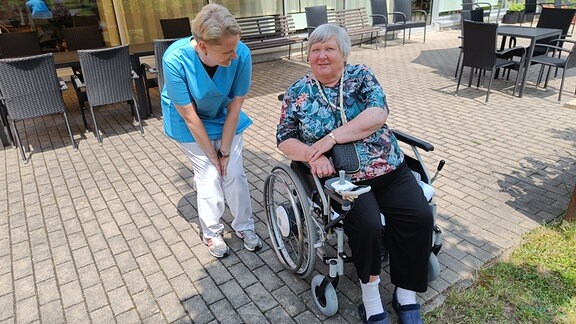 Pflegerin neben Seniorin im Rollstuhl