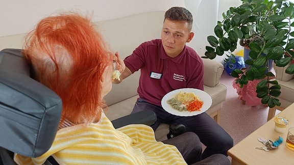 Pfleger füttert Seniorin im Rollstuhl