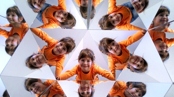 Ein Mädchen in kaleidoskopartigen Mustern, die durch drei zu einem Dreieck zusammengefügte Spiegel entstehen