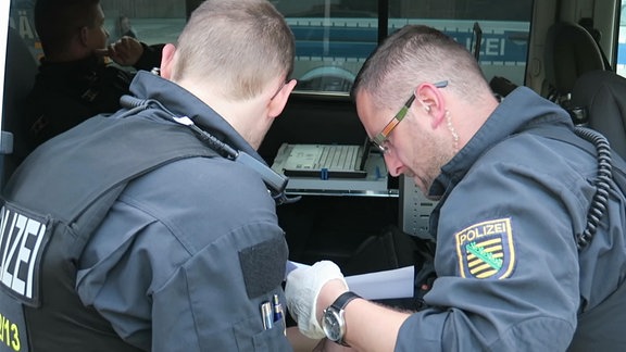 Zwei Polizisten überprüfen in einem Fahrzeug Papiere