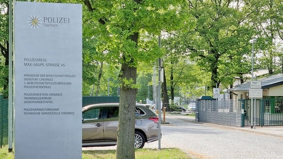 Ein Schild der Polizei Sachsen steht vor einem parkenden Auto.