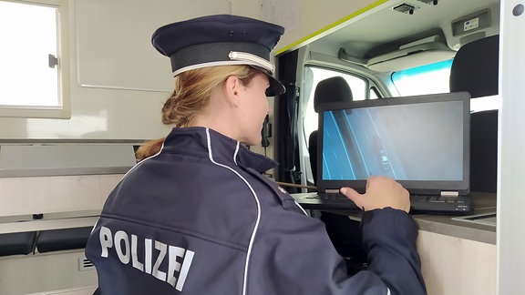 Polizistin blickt auf einen Monitor mit Luftaufnahme einer Autobahn.