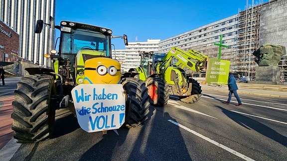 Zwei Traktoren mit Demo-Plakaten stehen auf einer Straße.