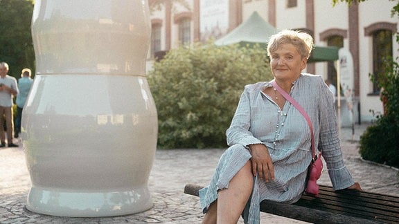 Die Künstlerin Uli Aigner sitzt in Lößnitz neben einem überlebensgroßen Porzellangefäß