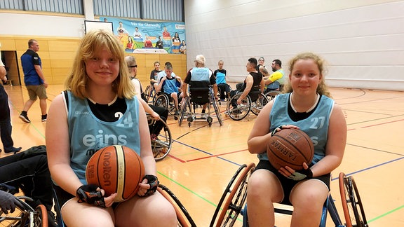 Zwei junge Frauen im Rollstuhl mit einen Basketball in den Händen.