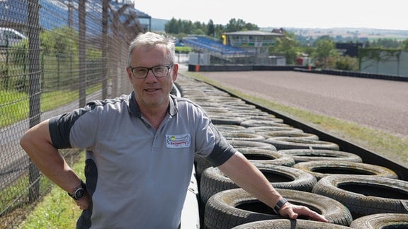 Ein Mann steht an der Rennstrecke auf einen Reifenstapel gestützt.