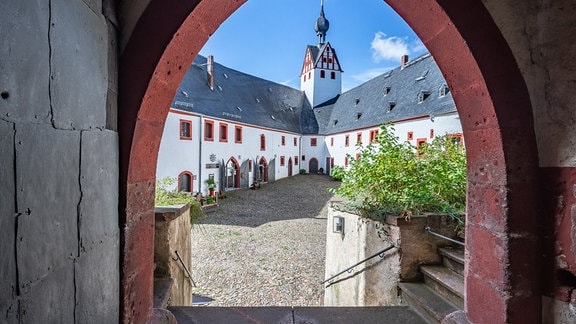 Durch einen mittelalterlichen Torbogen blickt man auf ein saniertes Schloss. Es ist Schloss Rochsburg bei Chemnitz.