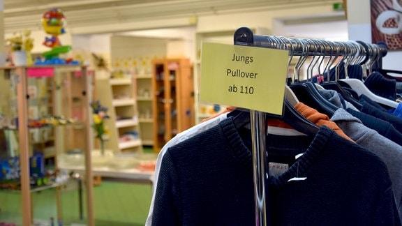An einem Kleiderständer in einem Verkaufsraum ein Schild: "Jungs Piullover ab 110".