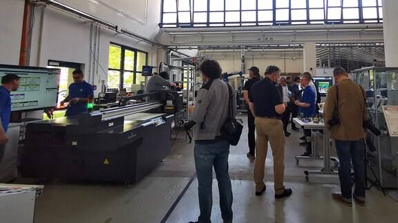 Blick in eine Produktionshalle mit verschiedenen Maschinen und Besuchern einer Führung.