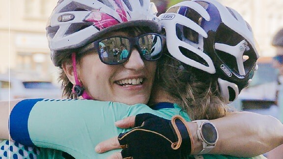 Zwei Radfahrerinnen umarmen sich.
