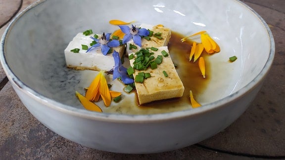 Mit Blüten und Kräutern verzierter Tofu auf einem Teller