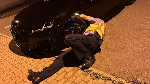Ein Polizist leuchtet liegend bei einer nächtlichen Fahrzeugkontrolle in ein Radhaus eines Audi TT RS.