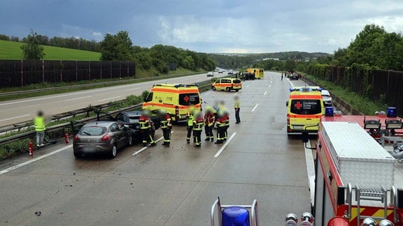 Rettungskräfte und Fahrzeuge stehen auf der Autobahn neben zwei Unfallautos.