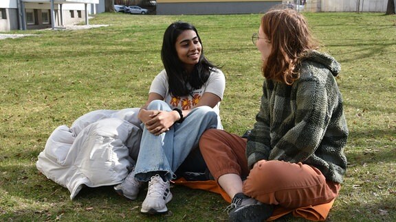 Sreelakshmi Sajeev und Hannah Weißenburger sitzen nebeneinander auf einer Wiese.