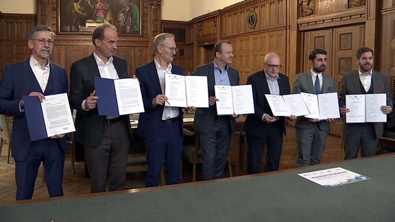 Sieben Männer stehen im Chemnitzer Rathaus mit Verträgen in der Hand nebeneinander.