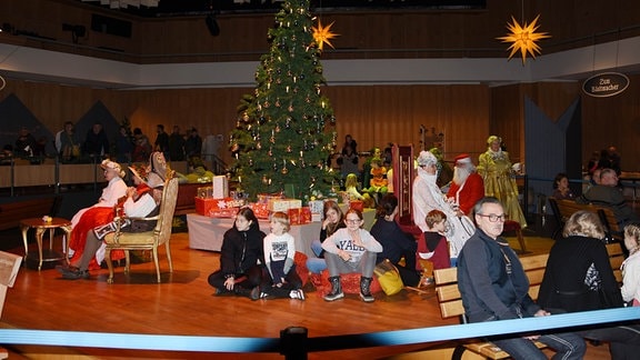 Ein Weihnachtsbaum, darum Weihnachtsmann, Eiskönigin und Kinder.