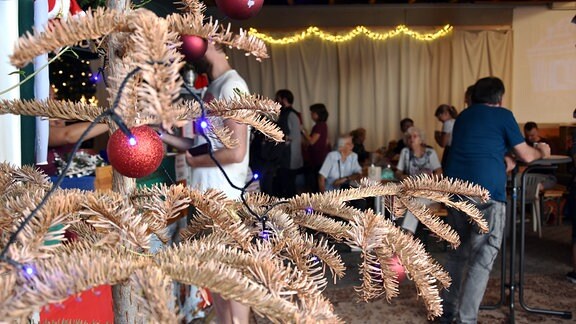 Ein Weihnachtsbaum mit braunen Nadeln, dahinter feiern Gäste