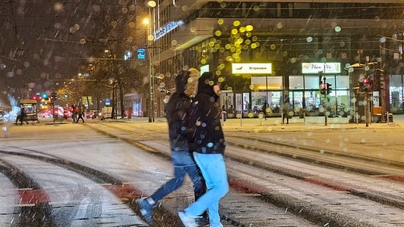 Zwei Menschen laufen über eine verschneite Straße in der Chemnitzer Innenstadt