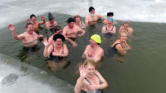 Männer und Frauen lachen und winken aus ihrer Eisbadestelle.