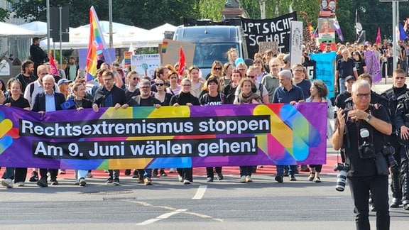 Auf einer Straße laufen Demo-Teilnehmer nebeneinander und tragen ein breites Transparent.