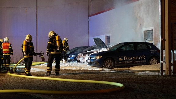 Feuerwehrleute löschen drei abgebrannte Autos.