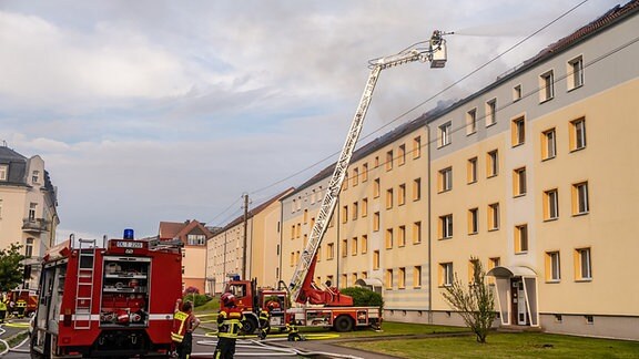 Ein Feuerwehrmann bekämpft auf einer Drehleiter den Dachstuhlbrand eines Mehrfamilienhauses