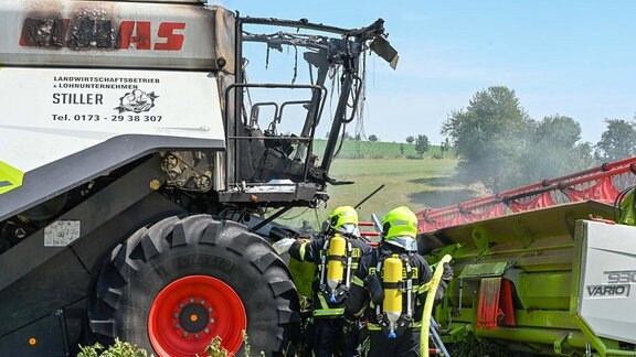 Zwei Feuerwehrleute löschen einen brennenden Mähdrescher.