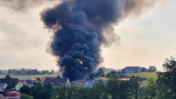 Dicke, dunkle Rauchwolken sind über einem Dorf zu sehen.