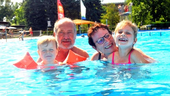 Eine Frau, ein Mann und zwei Kinder lachen im Wasser eines Schwimmbeckens.