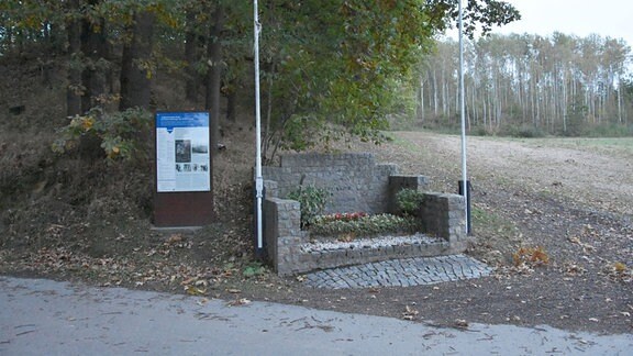 Ein Gedenkstein und eine Gedenktafel unter Bäumen am Ort des ehemaligen KZ bei Penig.