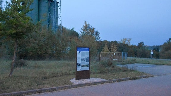 Eine Gedenktafel an einer Industriebrache in Penig mit einem alten Silo im Hintergrund.