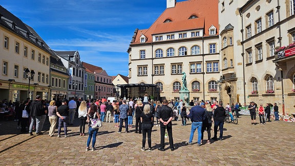 Auf dem Marktplatz in Döbeln stehen Menschen bei einem Göttesdienst vor einer Bühne neben dem Rathaus.