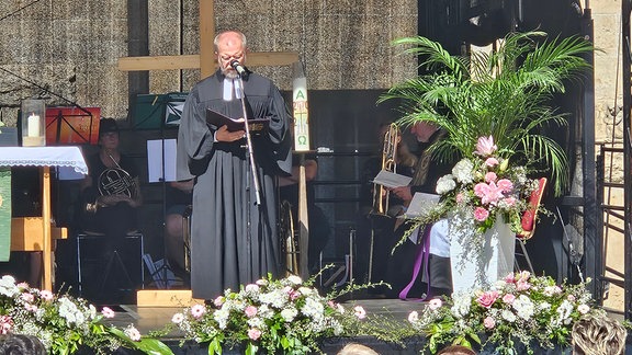Ein Pfarrer predigt auf einer Bühne.