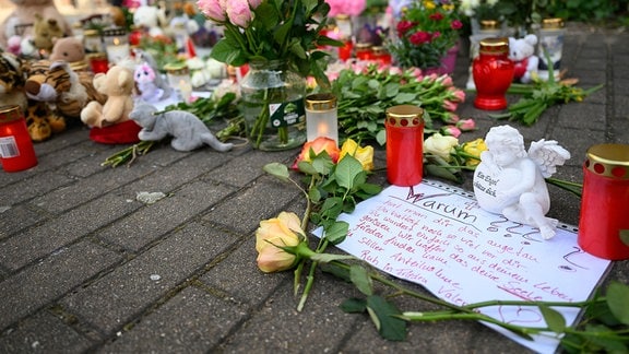 Blumen, Kerzen und ein Zettel mit der Aufschrift «Warum???» sind auf einem Fußweg abgelegt